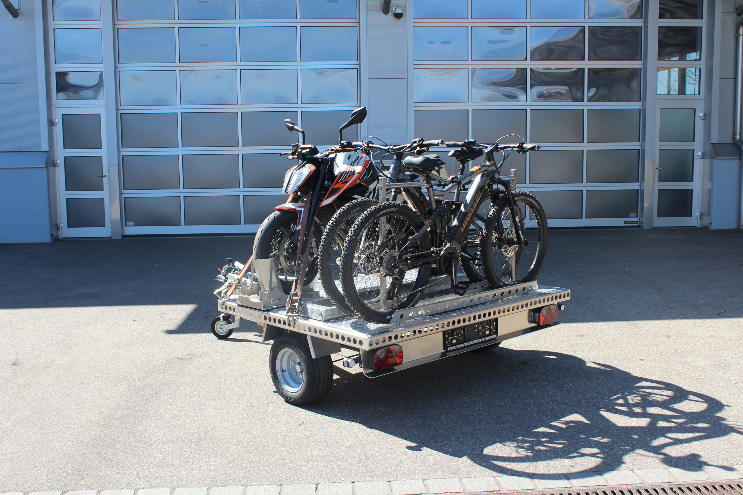 UA150 Quer Anhänger mit einer KTM Duke und zwei Fahrrädern beladen vor einer Halle