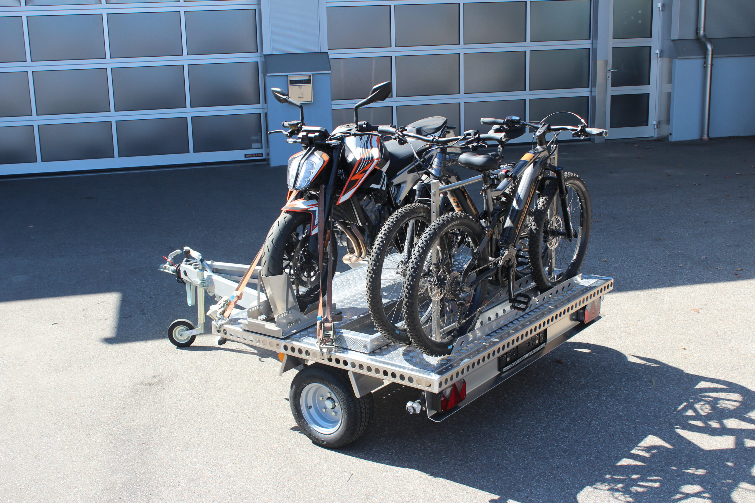 UA150 Quer Anhänger mit einer KTM Duke und zwei Fahrrädern beladen vor einer Halle