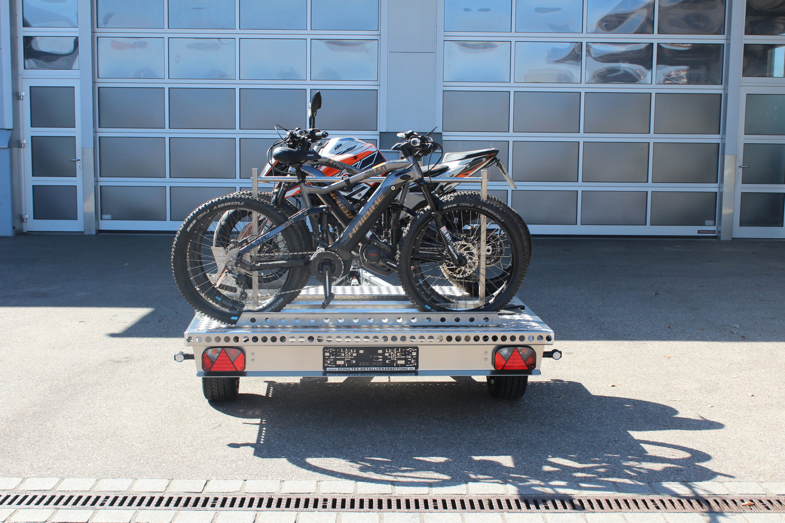 UA150 Quer Anhänger mit einer KTM Duke und zwei Fahrrädern beladen vor einer Halle