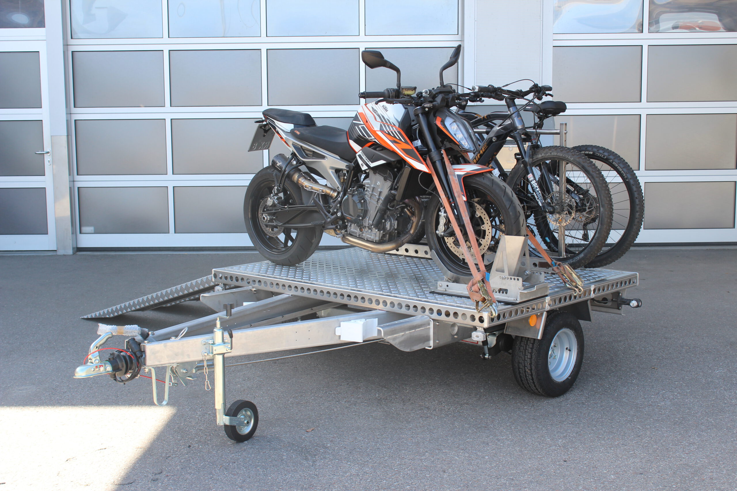 UA150 Quer Anhänger mit einer KTM Duke und zwei Fahrrädern beladen vor einer Halle