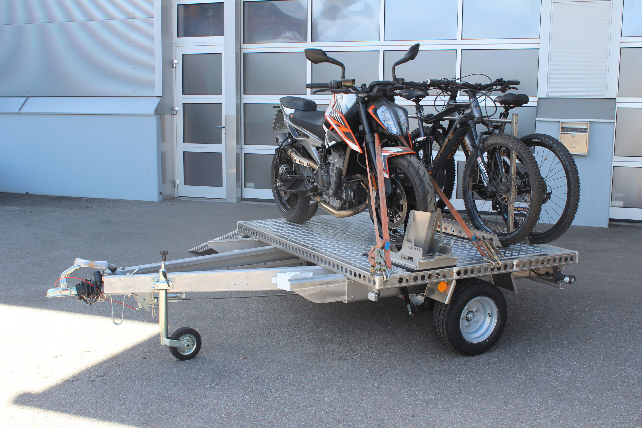UA150 Quer Anhänger mit einer KTM Duke und zwei Fahrrädern beladen vor einer Halle