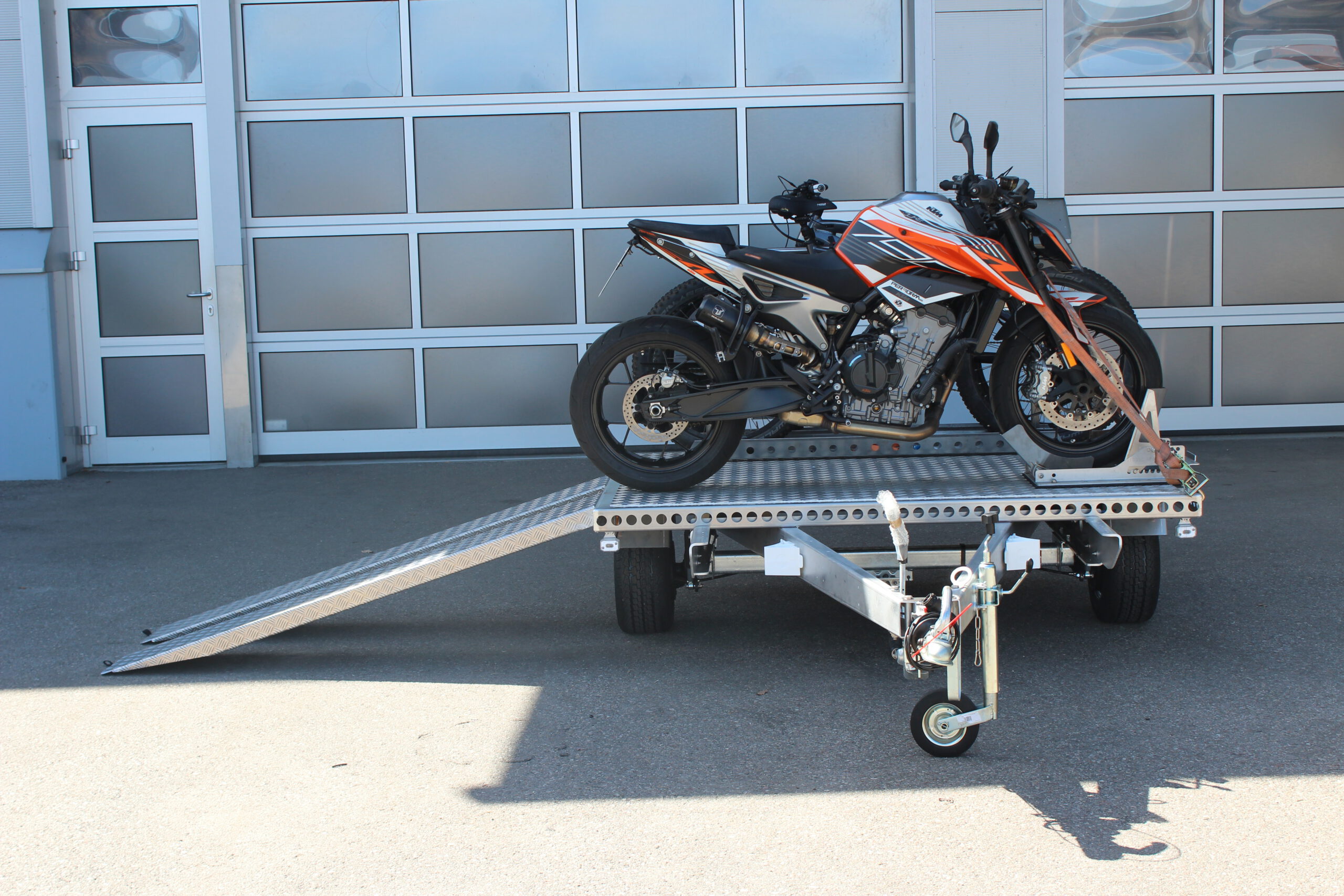 UA150 Quer Anhänger mit einer KTM Duke und zwei Fahrrädern beladen vor einer Halle