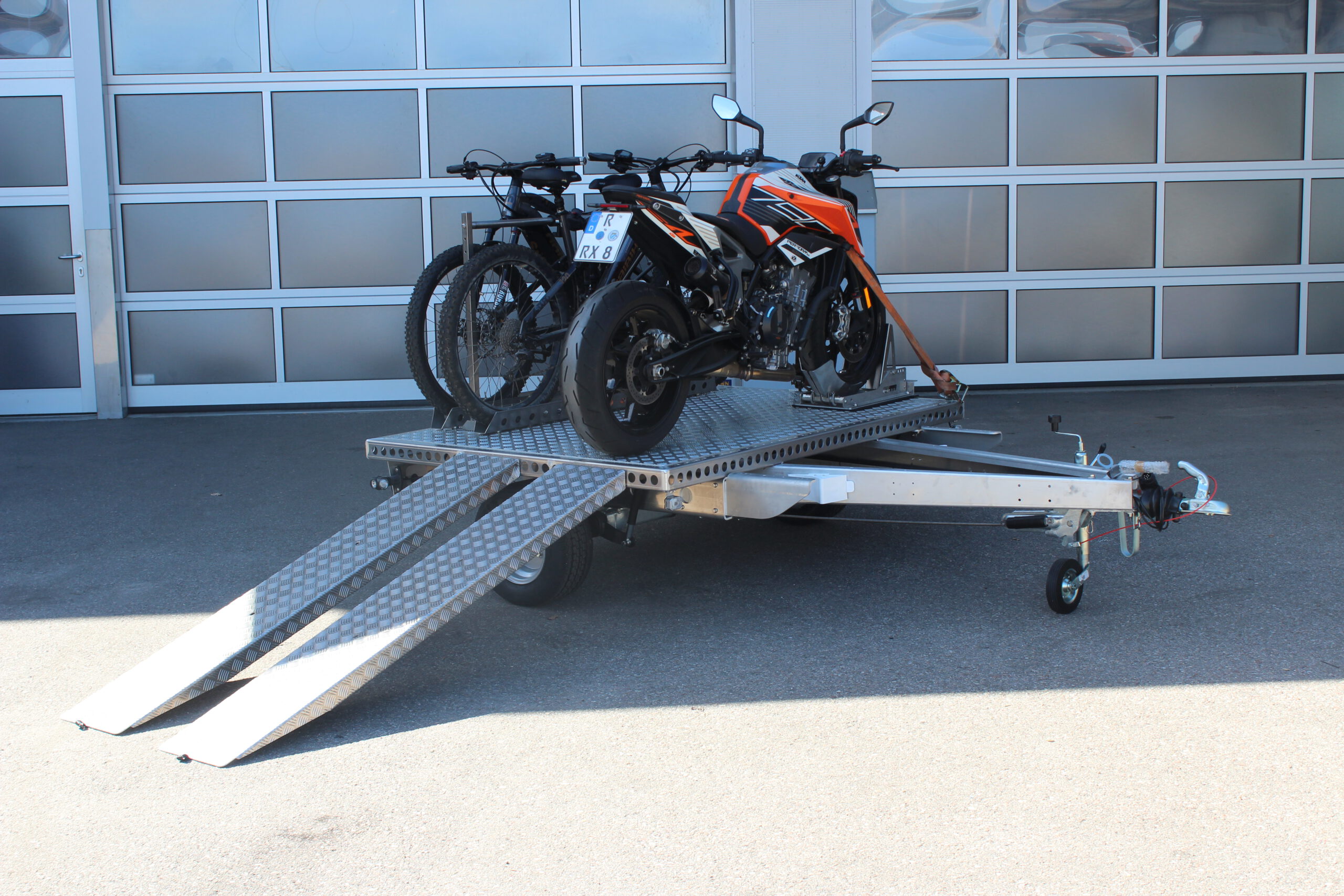 UA150 Quer Anhänger mit einer KTM Duke und zwei Fahrrädern beladen vor einer Halle