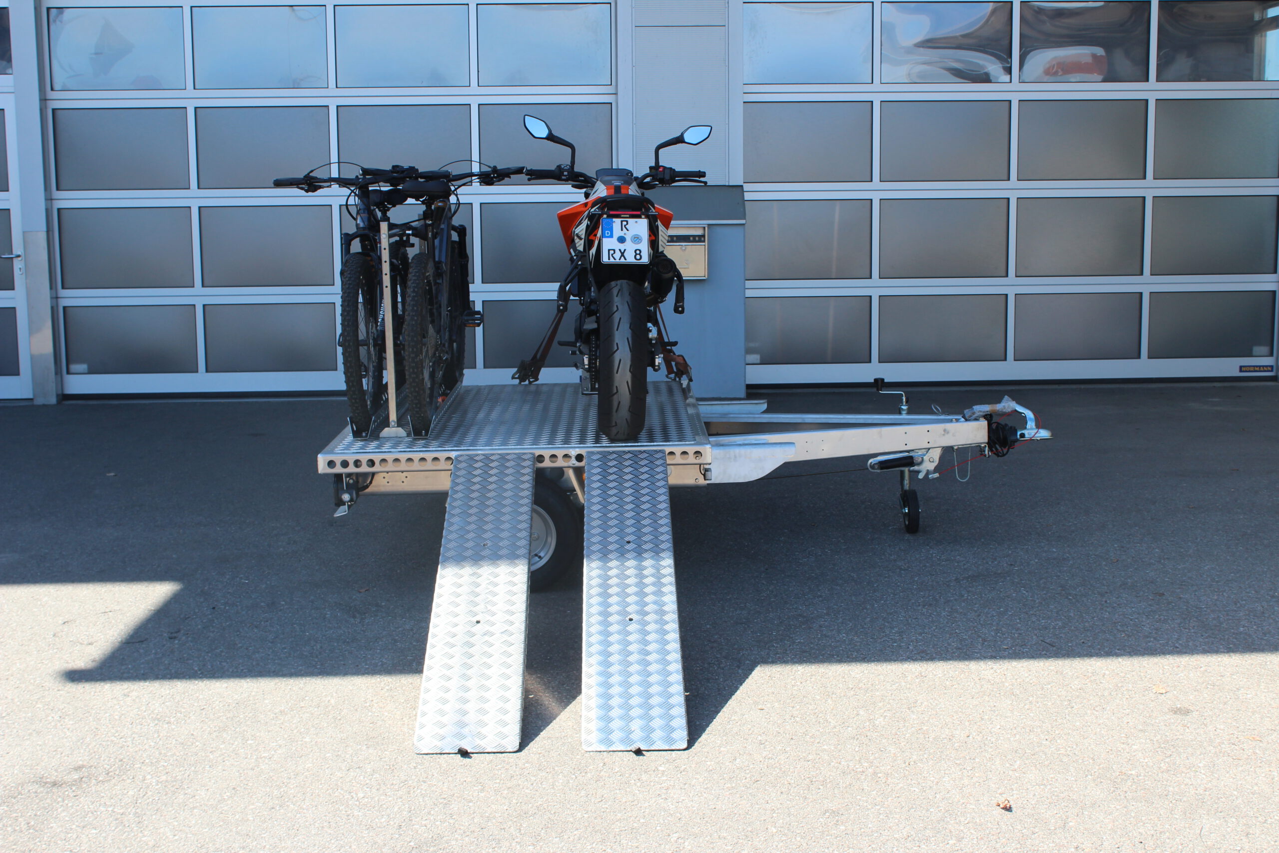 UA150 Quer Anhänger mit einer KTM Duke und zwei Fahrrädern beladen vor einer Halle