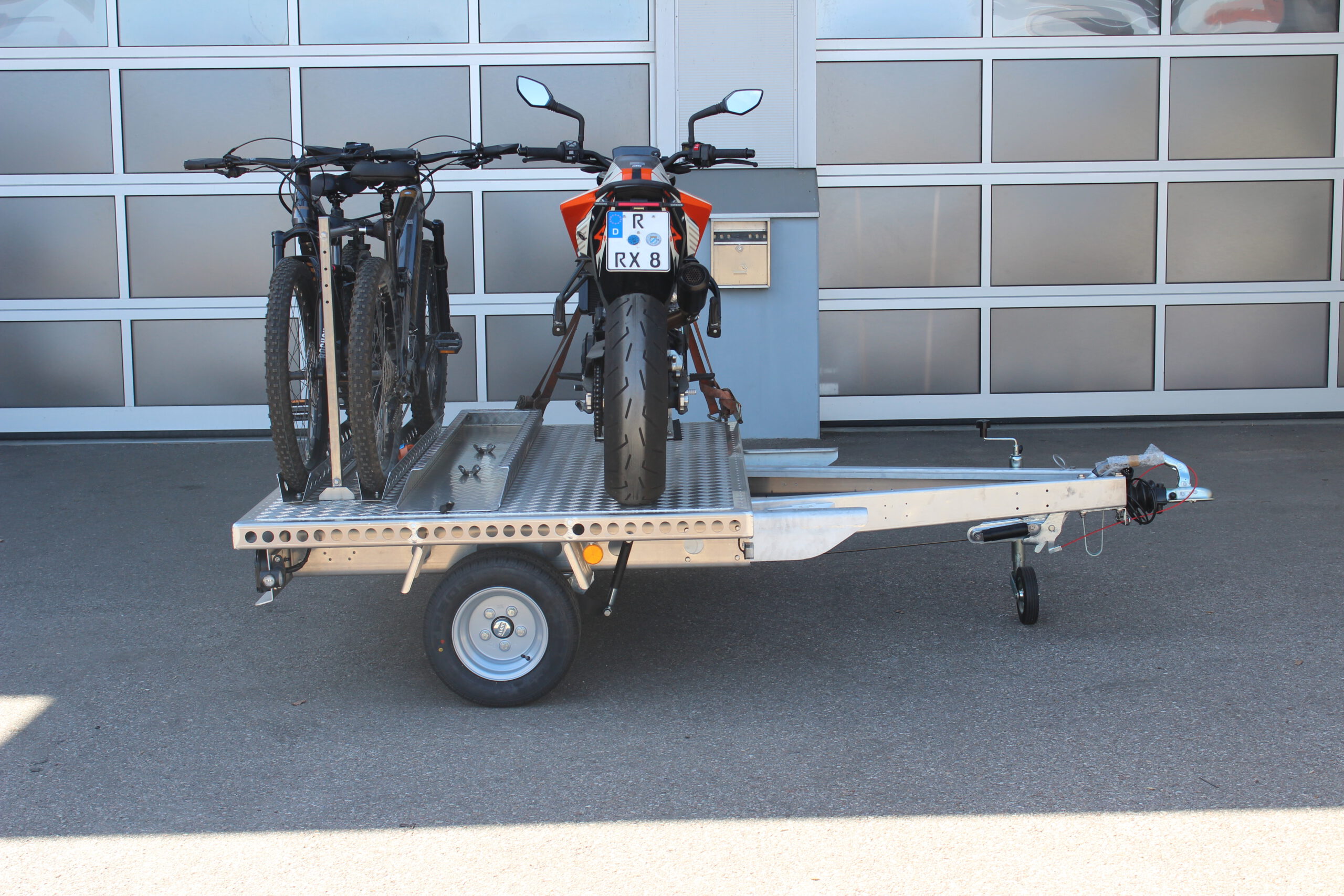 UA150 Quer Anhänger mit einer KTM Duke und zwei Fahrrädern beladen vor einer Halle