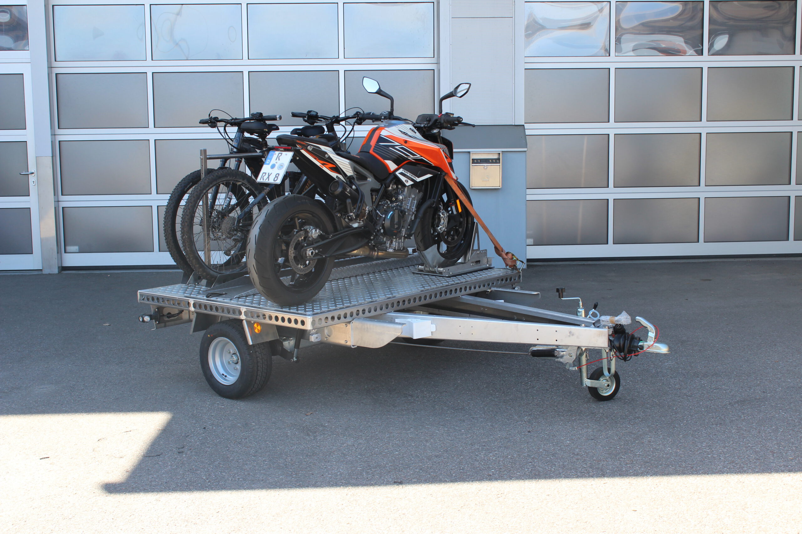 UA150 Quer Anhänger mit einer KTM Duke und zwei Fahrrädern beladen vor einer Halle