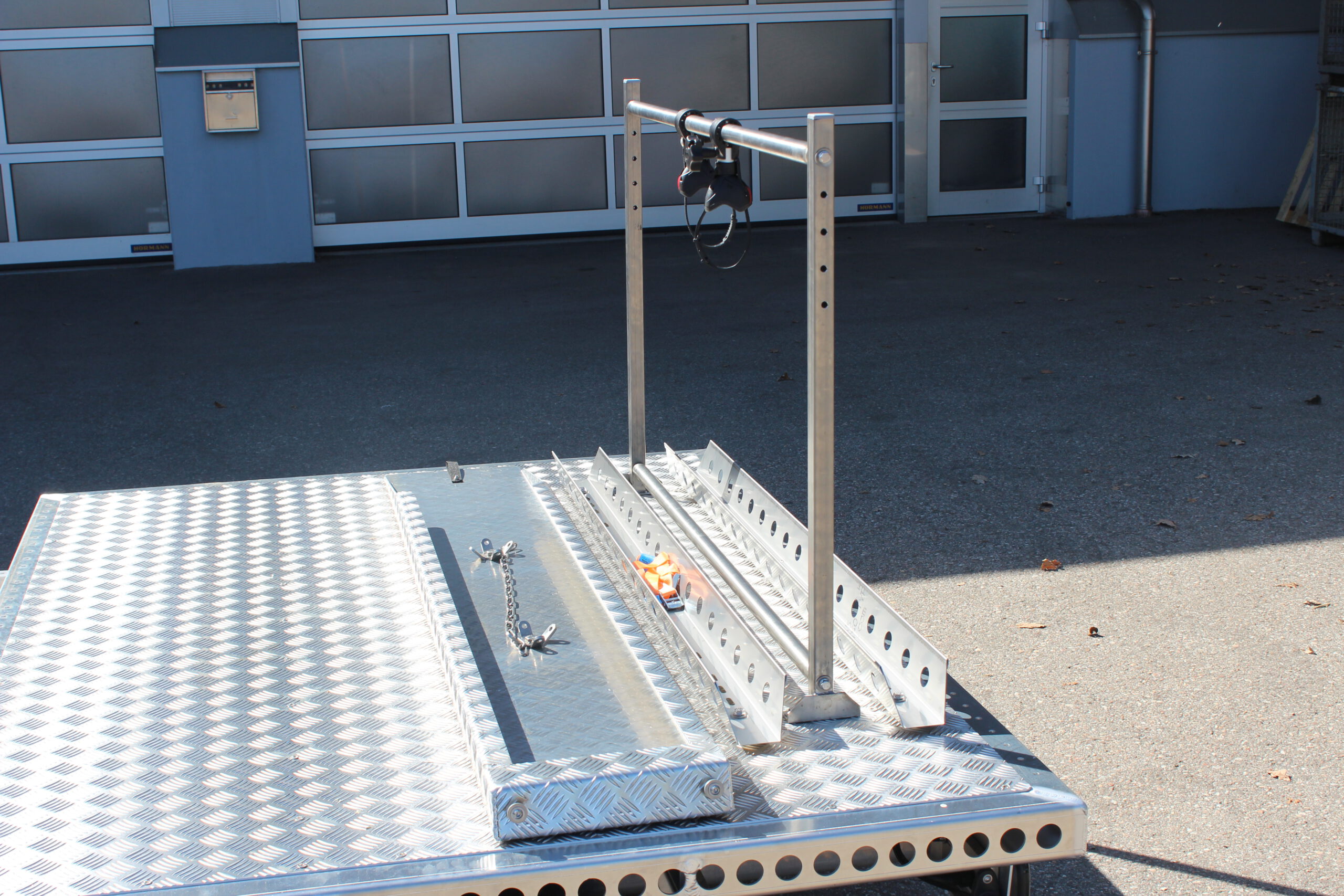 UA150 Quer Anhänger auf Aluminium mit einem Fahrradträger und einer Auffahrrampe auf der Plattform Vor einer Halle