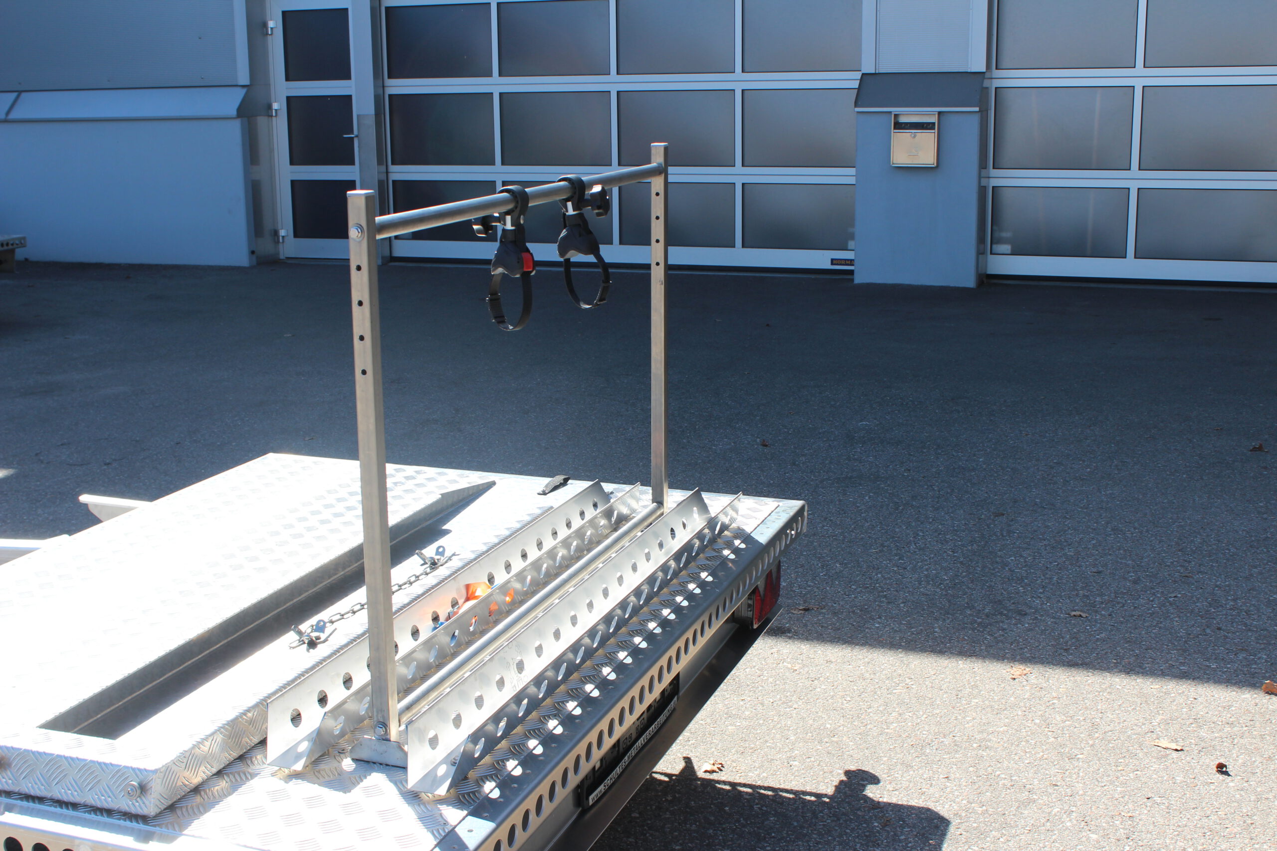 UA150 Quer Anhänger auf Aluminium mit einem Fahrradträger und einer Auffahrrampe auf der Plattform Vor einer Halle