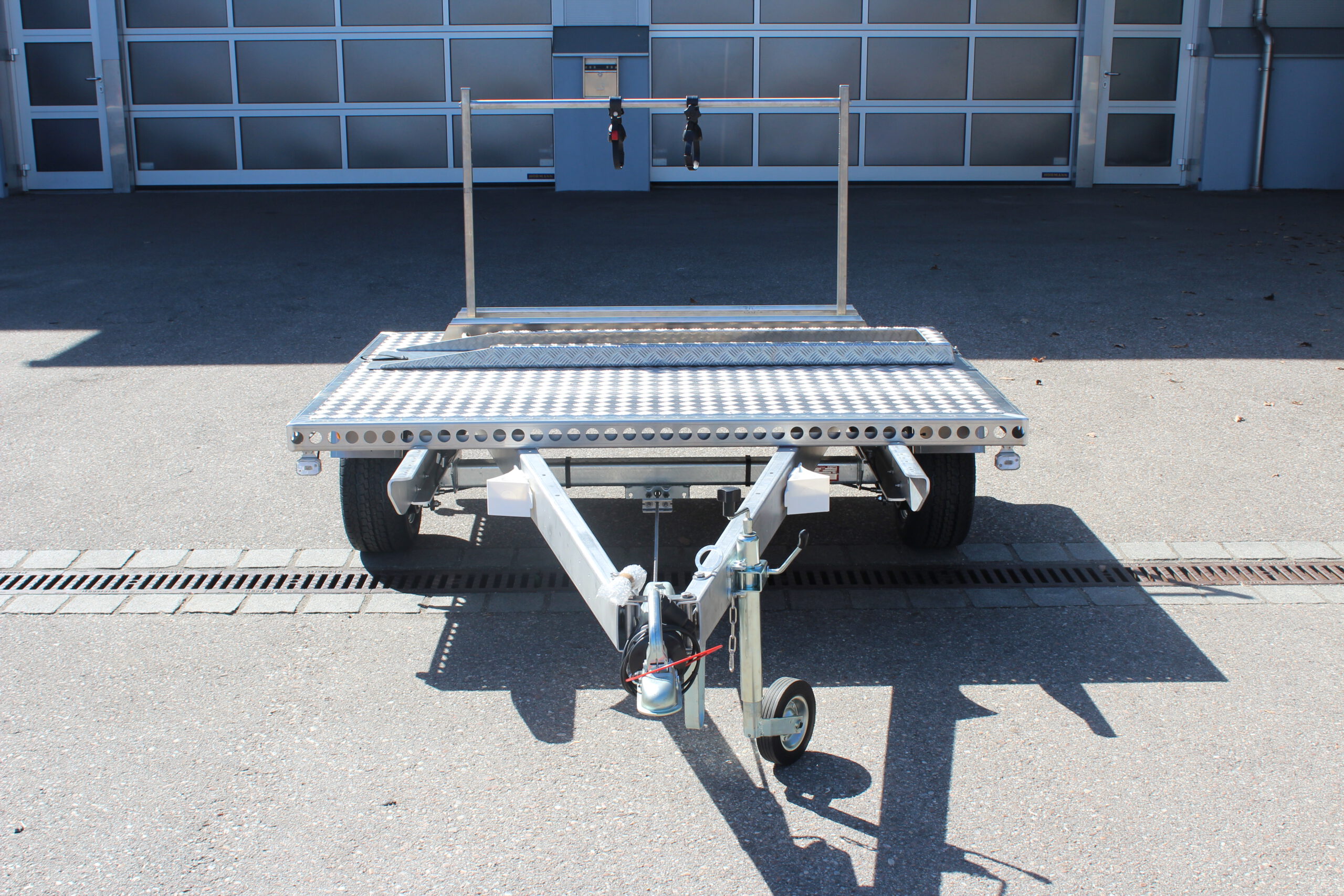 UA150 Quer Anhänger auf Aluminium mit einem Fahrradträger und einer Auffahrrampe auf der Plattform Vor einer Halle