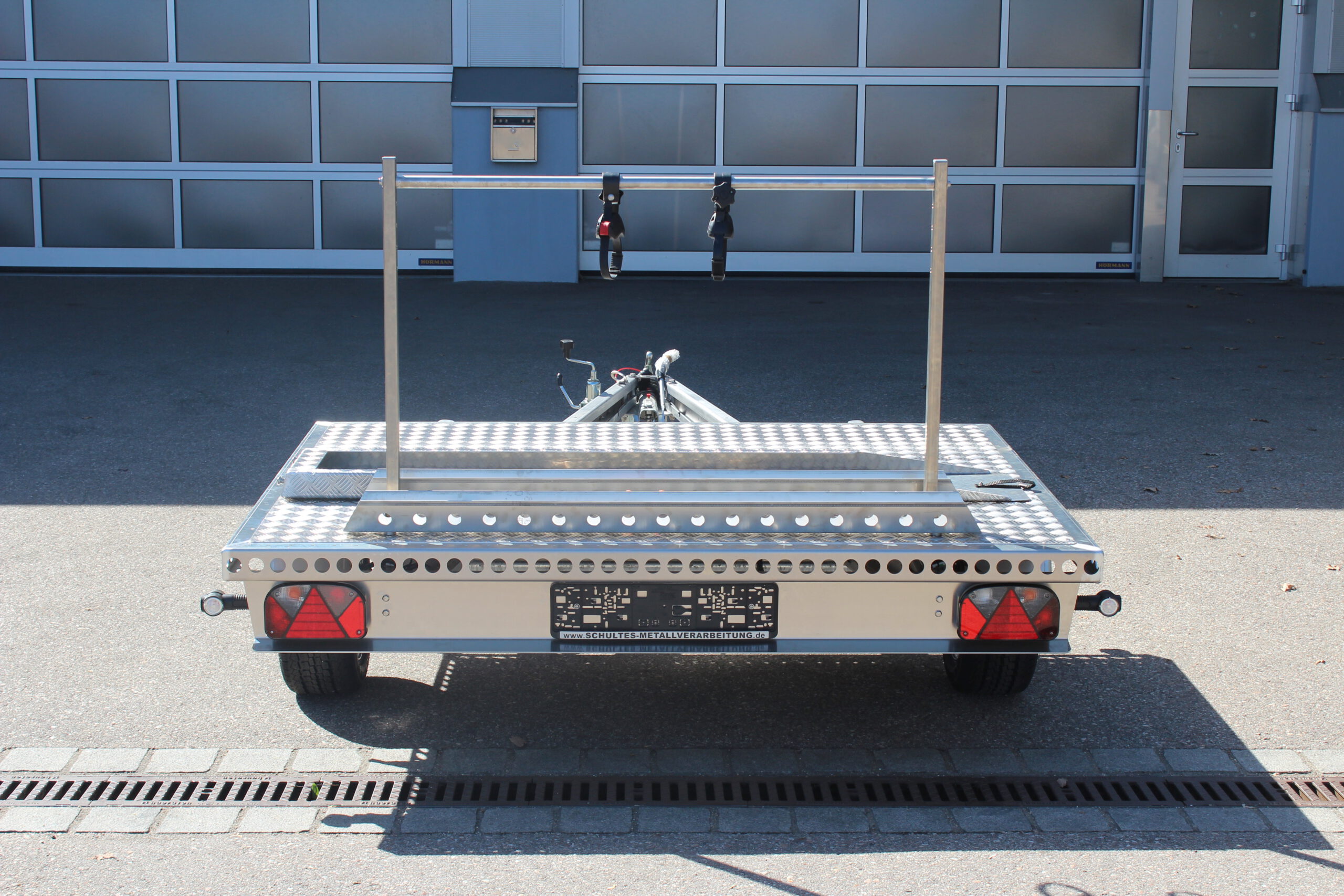 UA150 Quer Anhänger auf Aluminium mit einem Fahrradträger und einer Auffahrrampe auf der Plattform Vor einer Halle