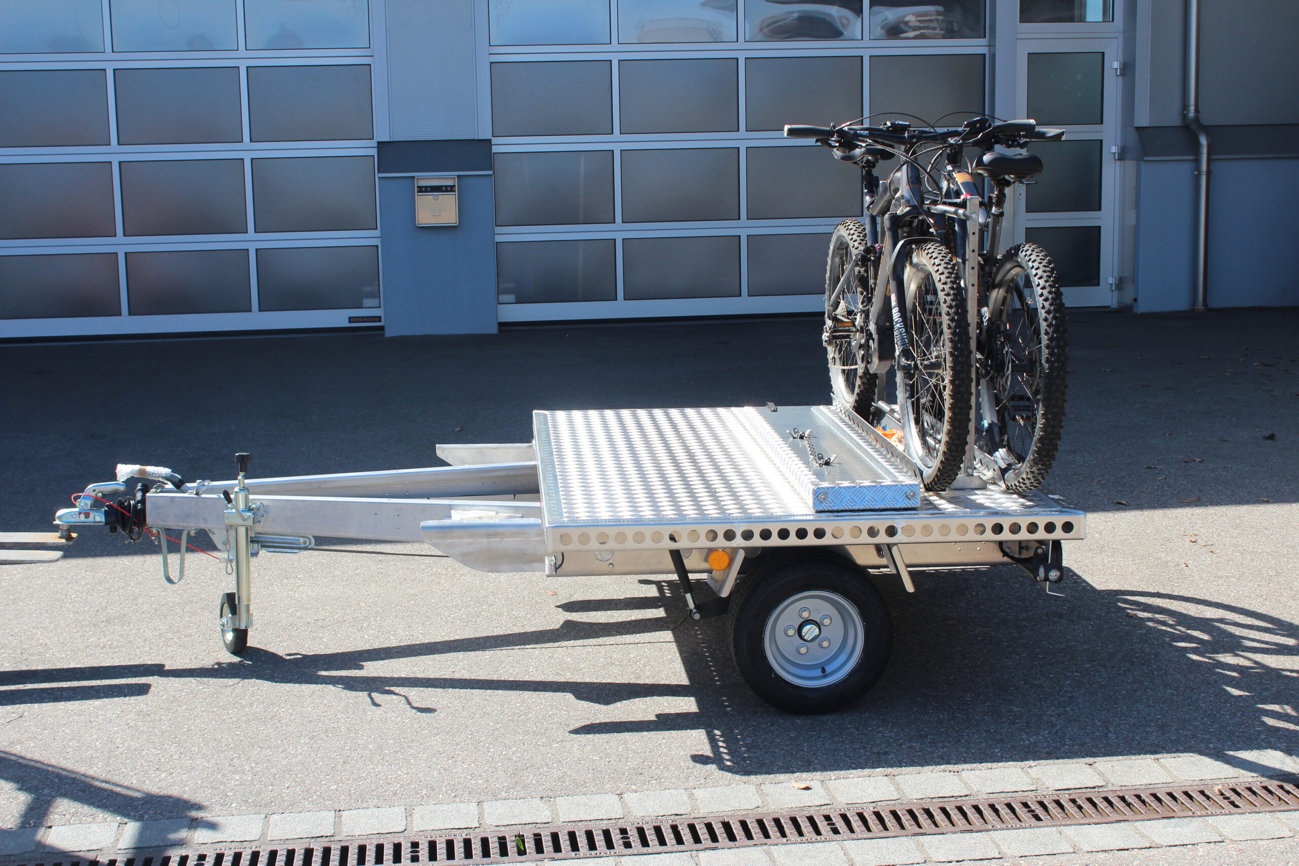 UA150 Quer Anhänger mit zwei Fahrrädern beladen. Vor einer Halle