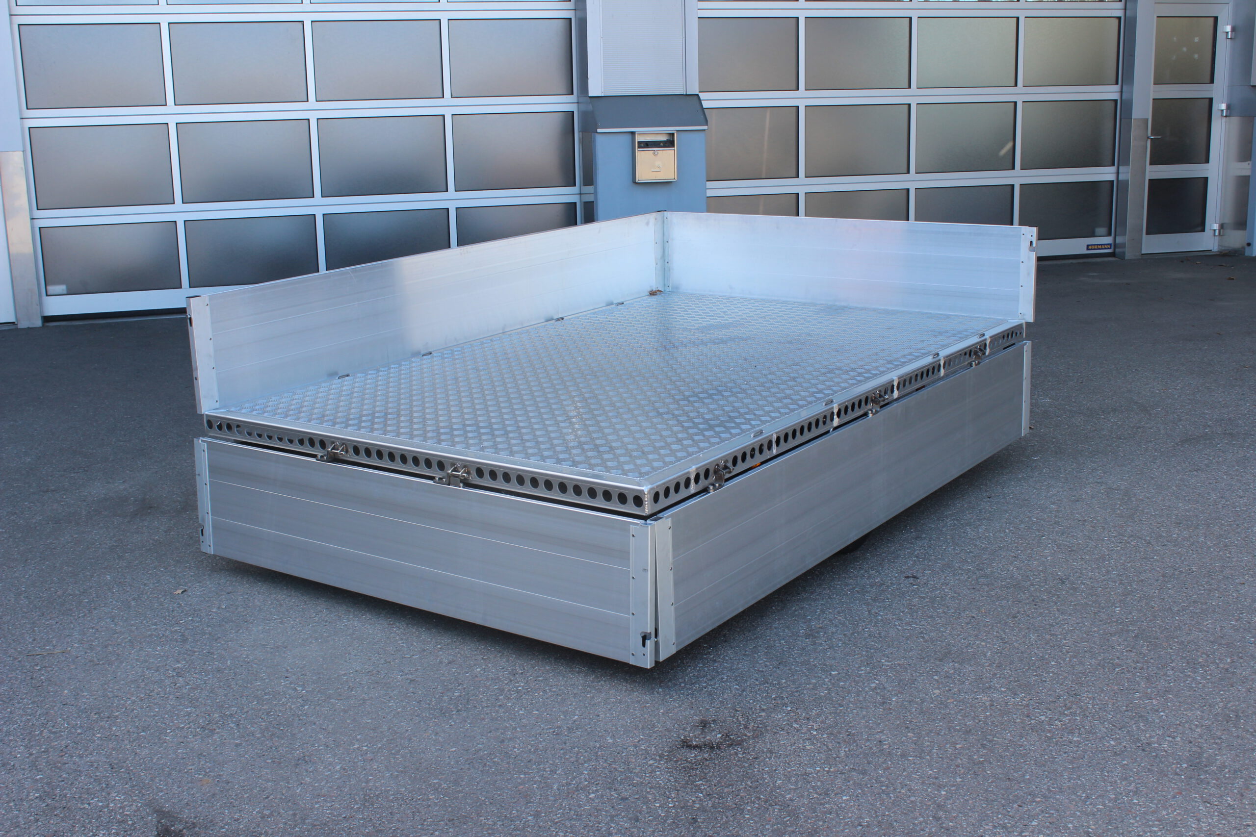 Aluminium Anhänger mit Alu Bordwänden umlaufend 40cm hoch vor einer Halle
