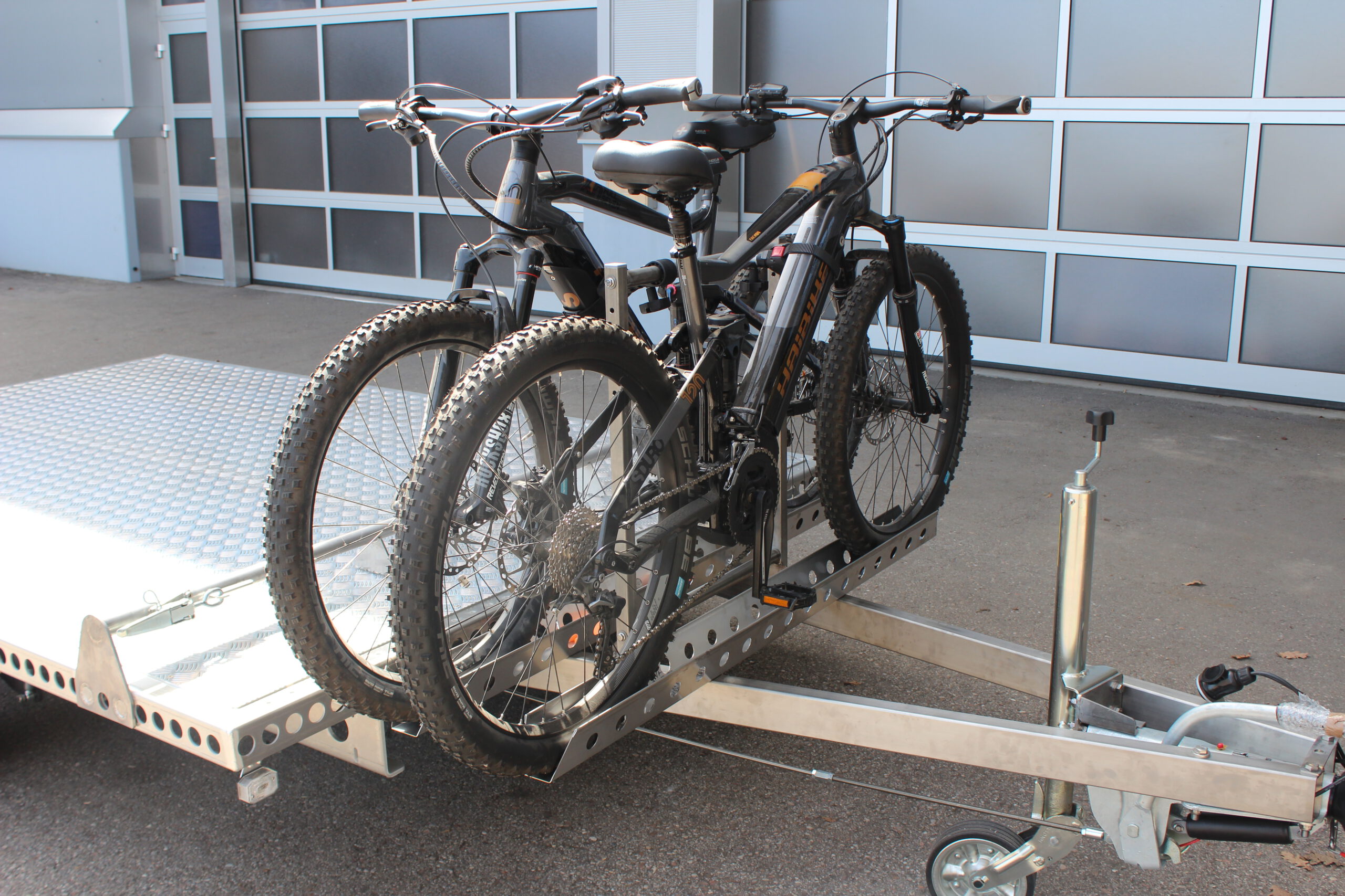 Aluminium Anhänger mit einem Edelstahl Fahrradträger mit 2 E-Bikes auf der Zugdeichsel vor einer Halle
