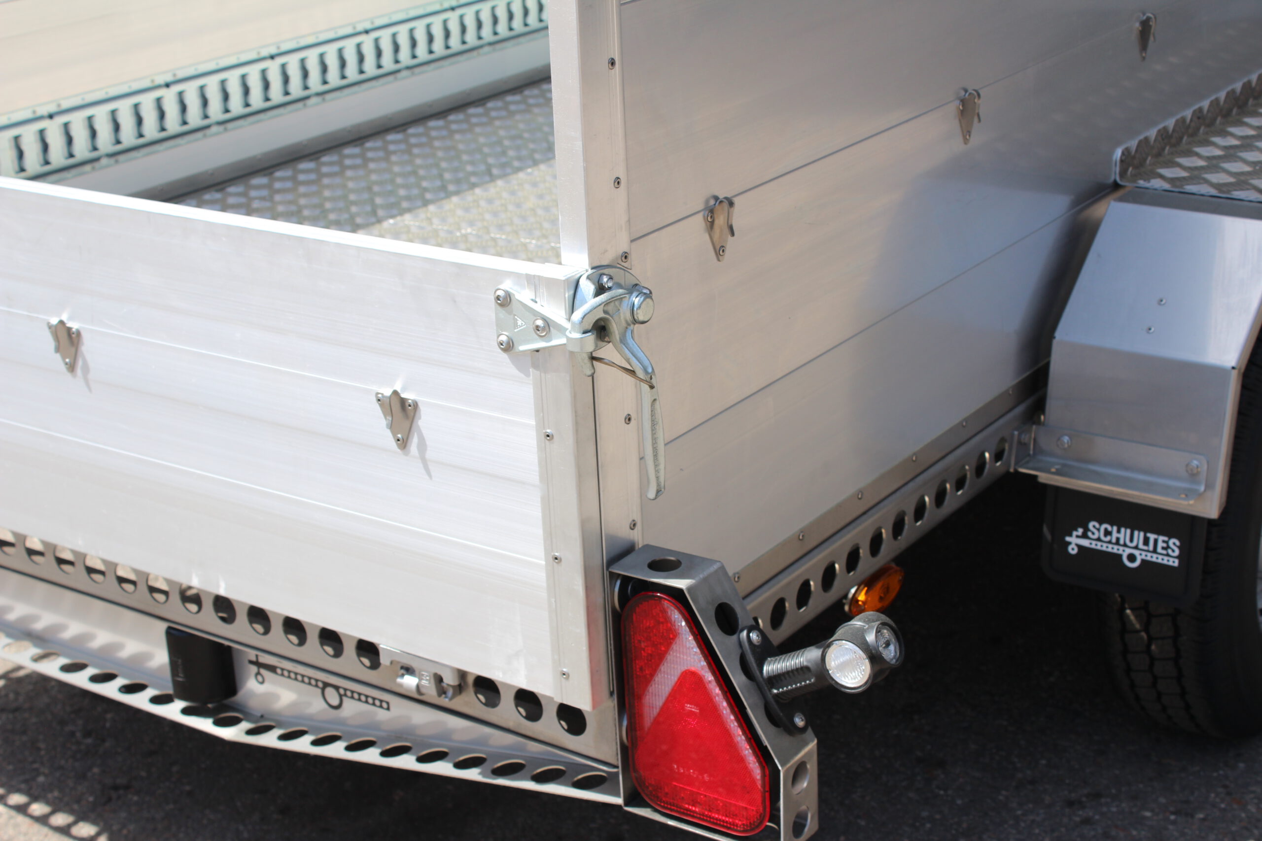 Edelstahl Tieflader Anhänger mit Aluminium Bordwänden für den gewerblichen Einsatz. Zweiachser aus Edelstahl mit Heckklappe vor einer Halle auf einem Hof