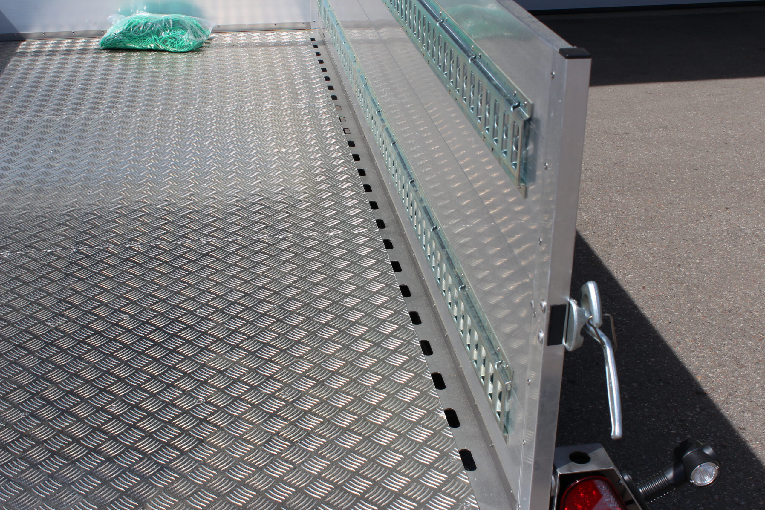 Edelstahl Tieflader Anhänger mit Aluminium Bordwänden für den gewerblichen Einsatz. Zweiachser aus Edelstahl mit Heckklappe vor einer Halle auf einem Hof