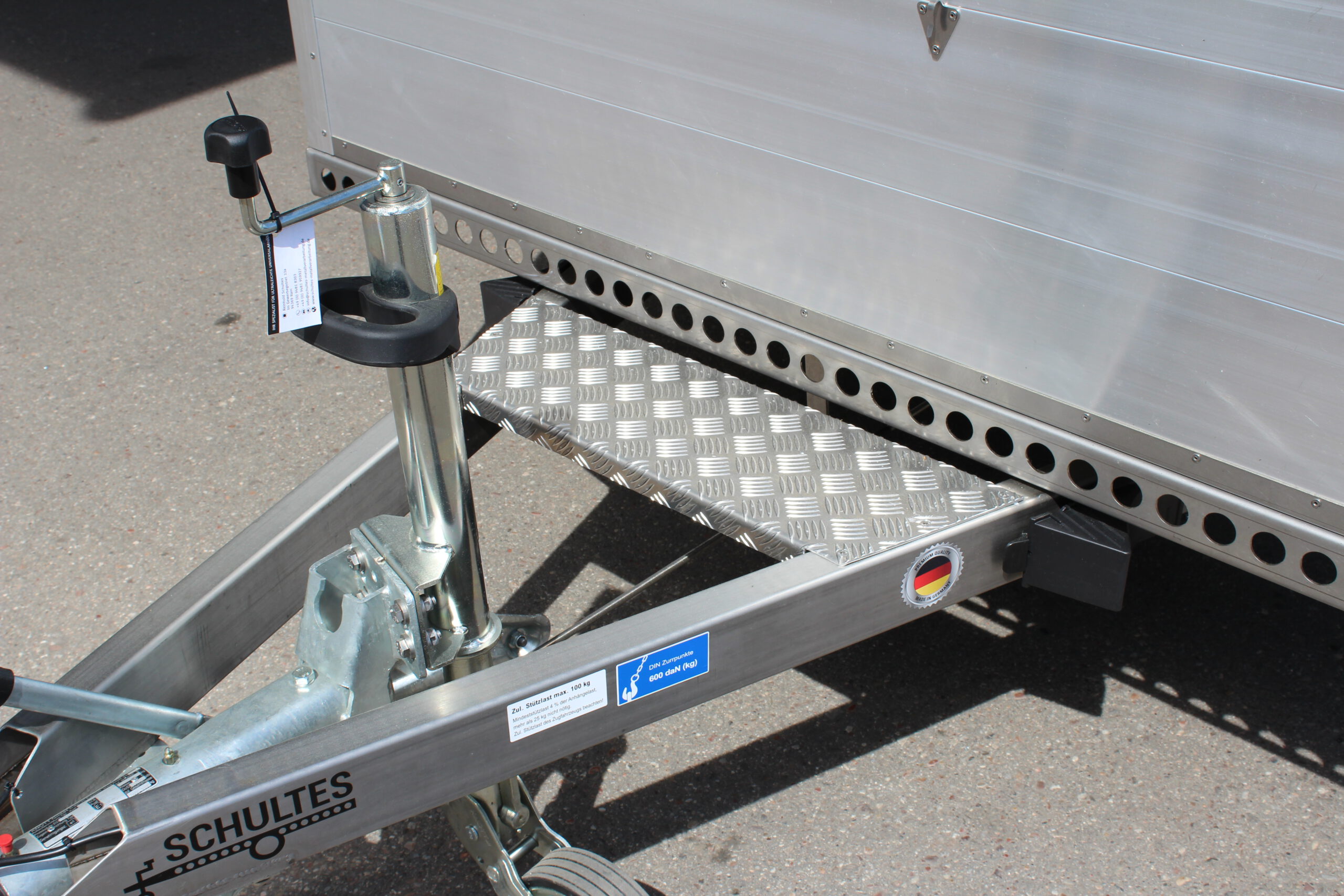 Edelstahl Tieflader Anhänger mit Aluminium Bordwänden für den gewerblichen Einsatz. Zweiachser aus Edelstahl mit Heckklappe vor einer Halle auf einem Hof