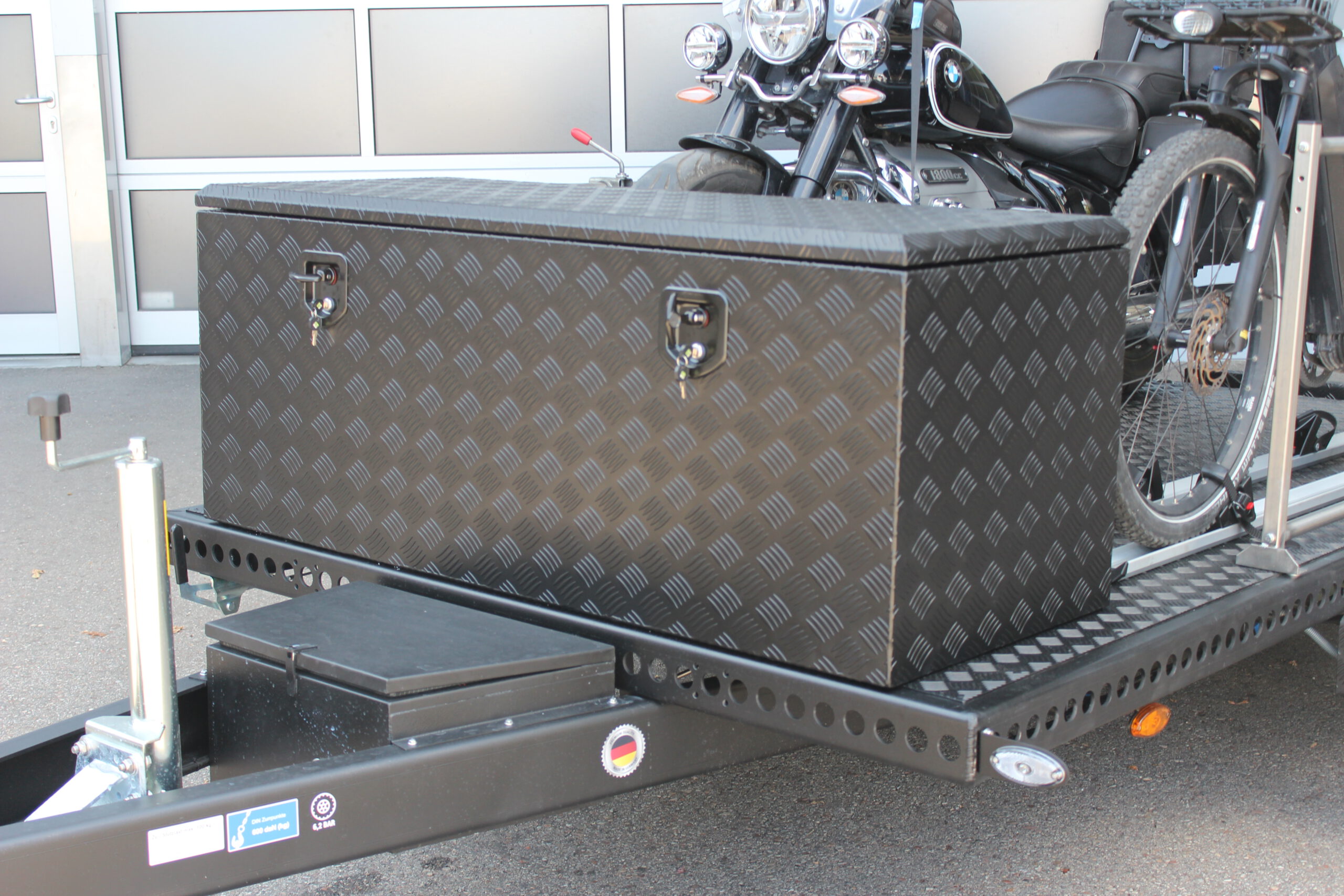 Große Aluminium Transportbox vorne quer auf einem Anhänger montiert, schwarz lackiert