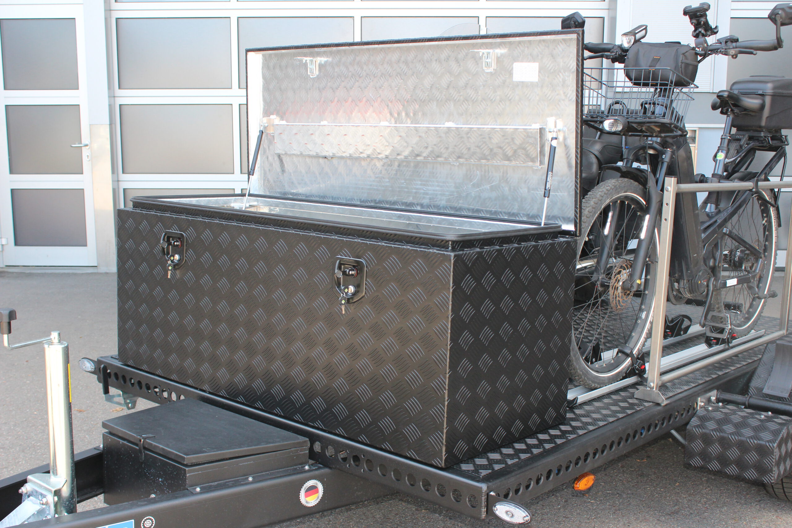 Große Aluminium Transportbox vorne quer auf einem Anhänger montiert, schwarz lackiert