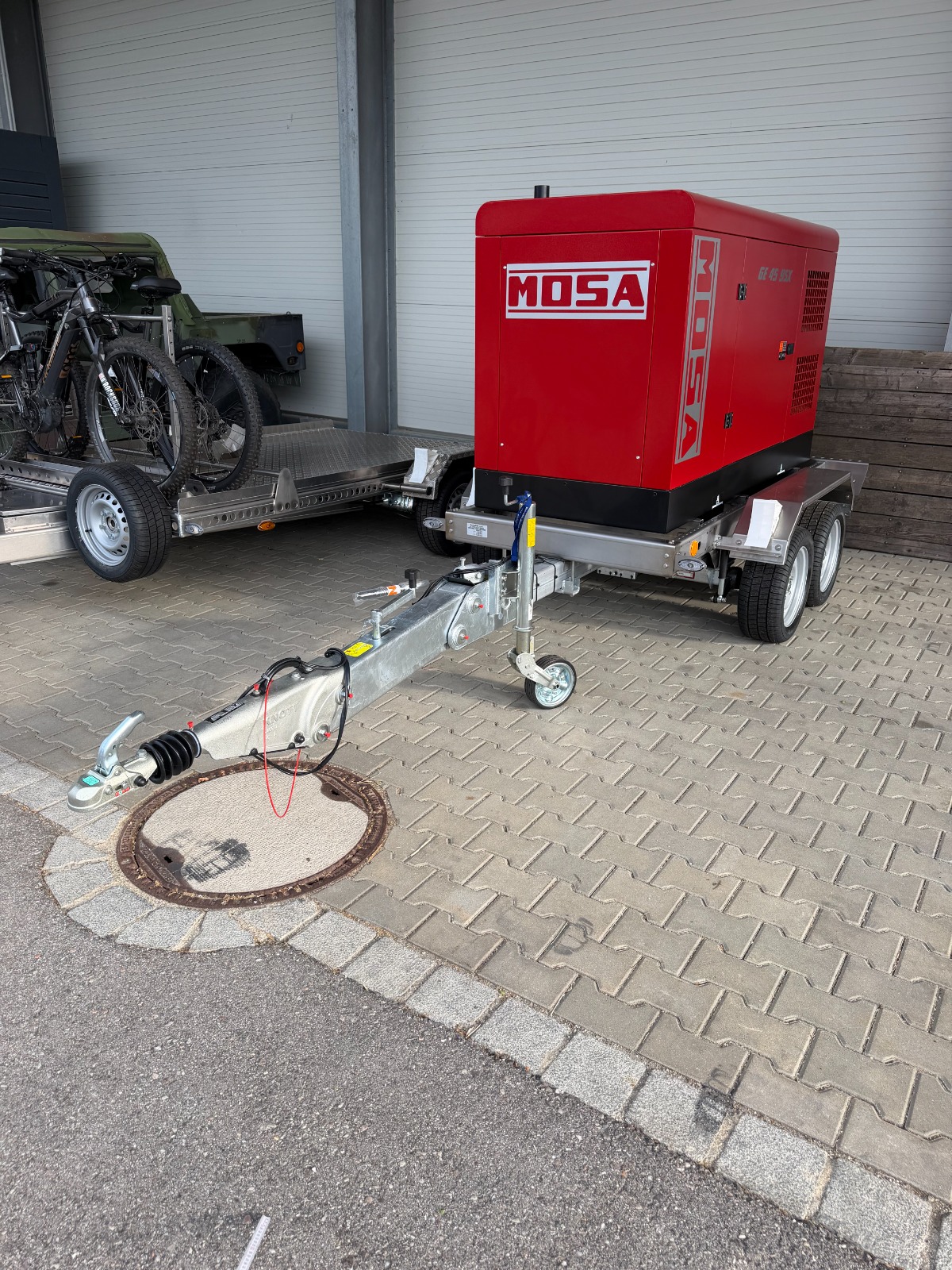 Edelstahl Fahrgestell mit höhenverstellbarer Zugdeichsel mit einem roten Stromaggregat beladen, unter einem Überdach