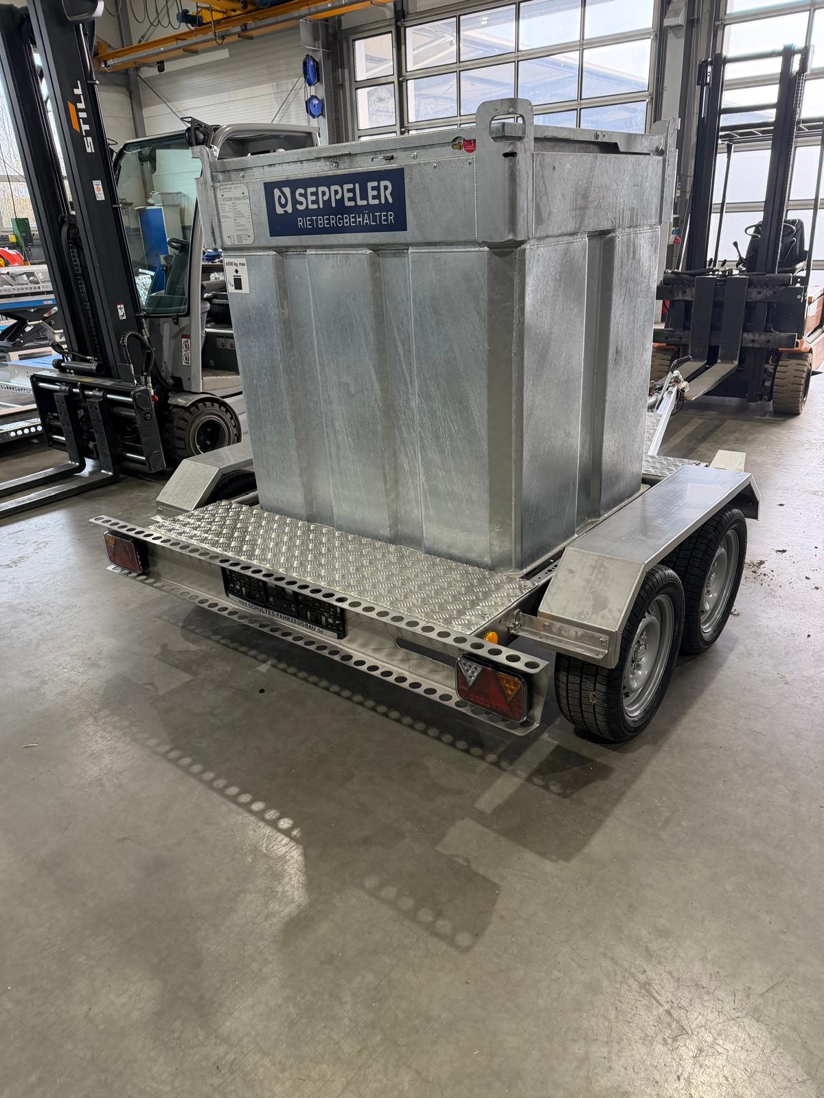Edelstahl Fahrgestell mit einem silbernen mobilen Dieseltank beladen, als mobile Tankstelle, in einer Halle mit Gabelstaplern im Hintergrund