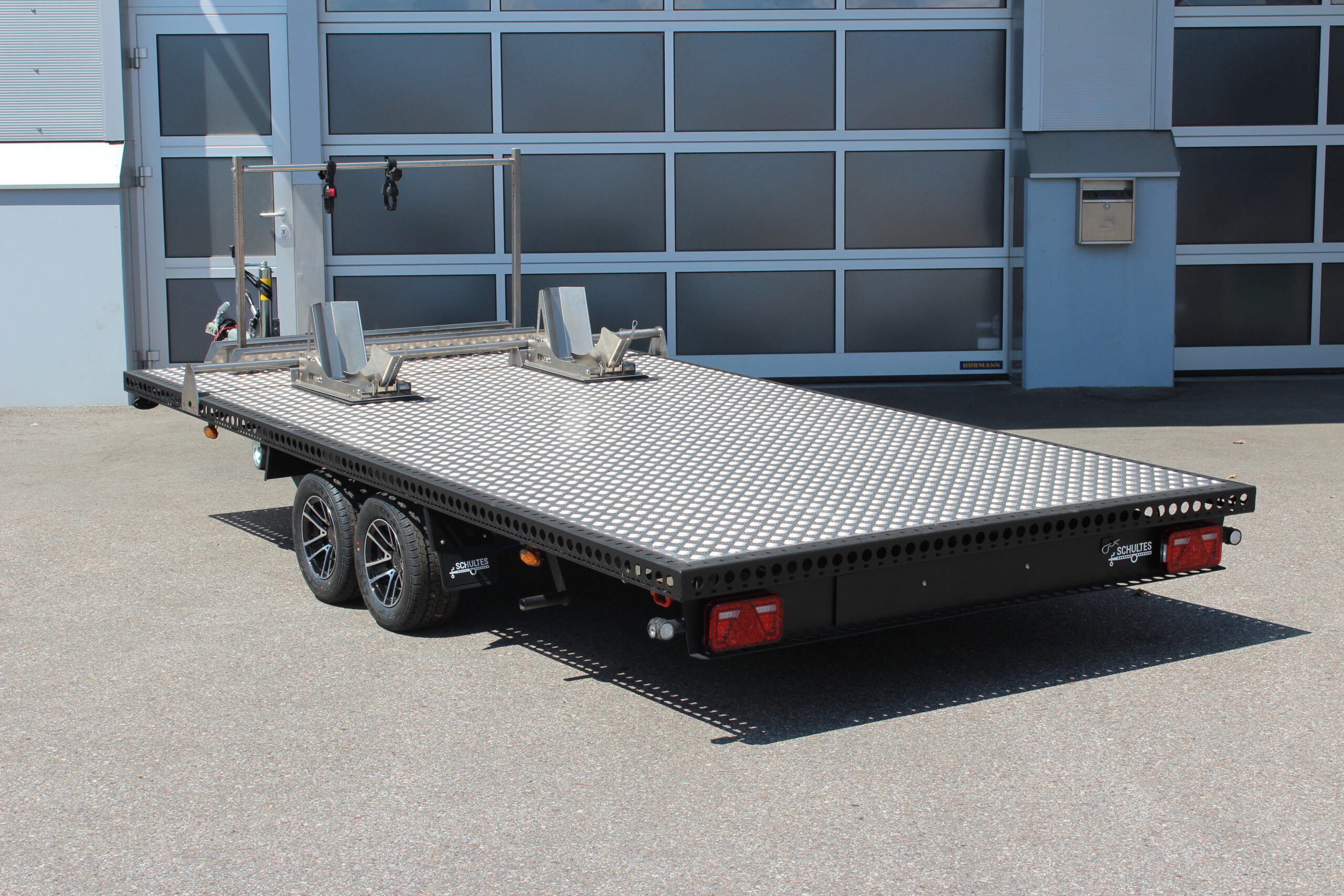 UA410 Edelstahl Anhänger schwarz lackiert mit silbernem Riffelblech. Mit einem Fahrradträger und zwei Radwippen beladen. Vor einem Hallentor in einem Hof