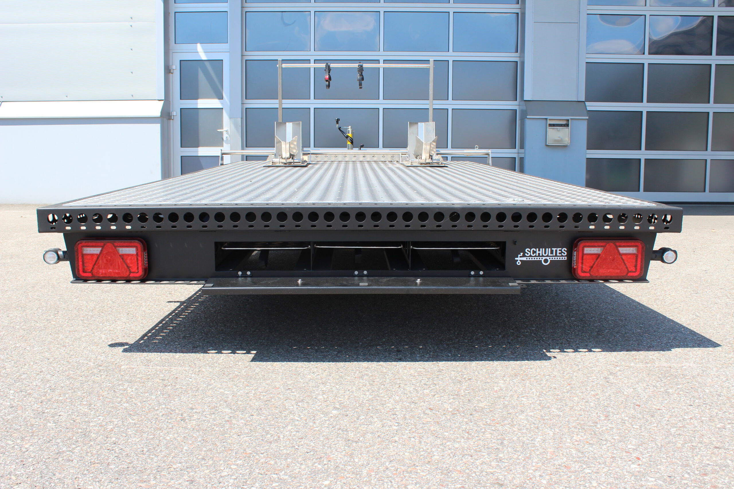 UA410 Edelstahl Anhänger schwarz lackiert mit silbernem Riffelblech. Mit einem Fahrradträger und zwei Radwippen beladen. Vor einem Hallentor in einem Hof