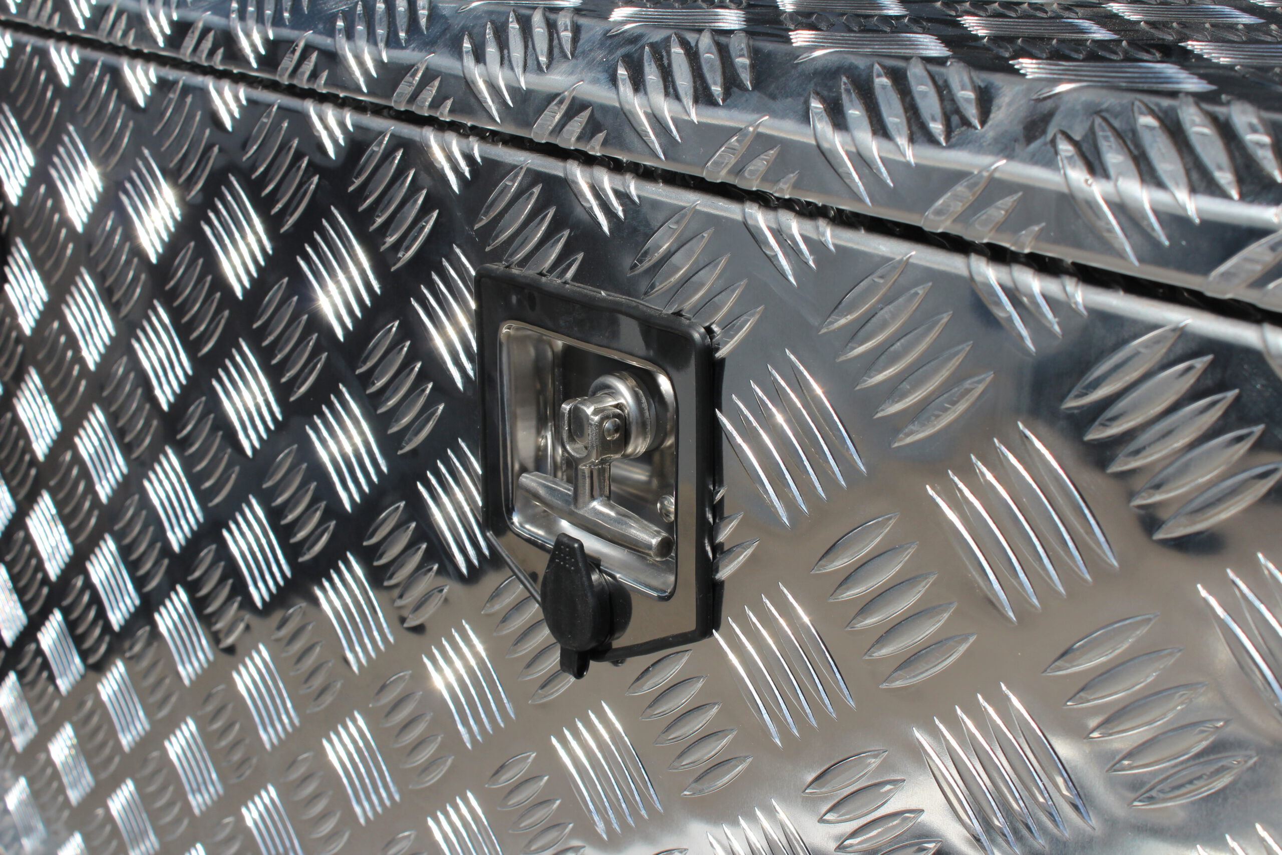 Große silberne Aluminium Riffelblech Staubox mit zwei Drehverschlüssen. Steht auf einem silbernen Aluminium Anhänger vor einem Tor