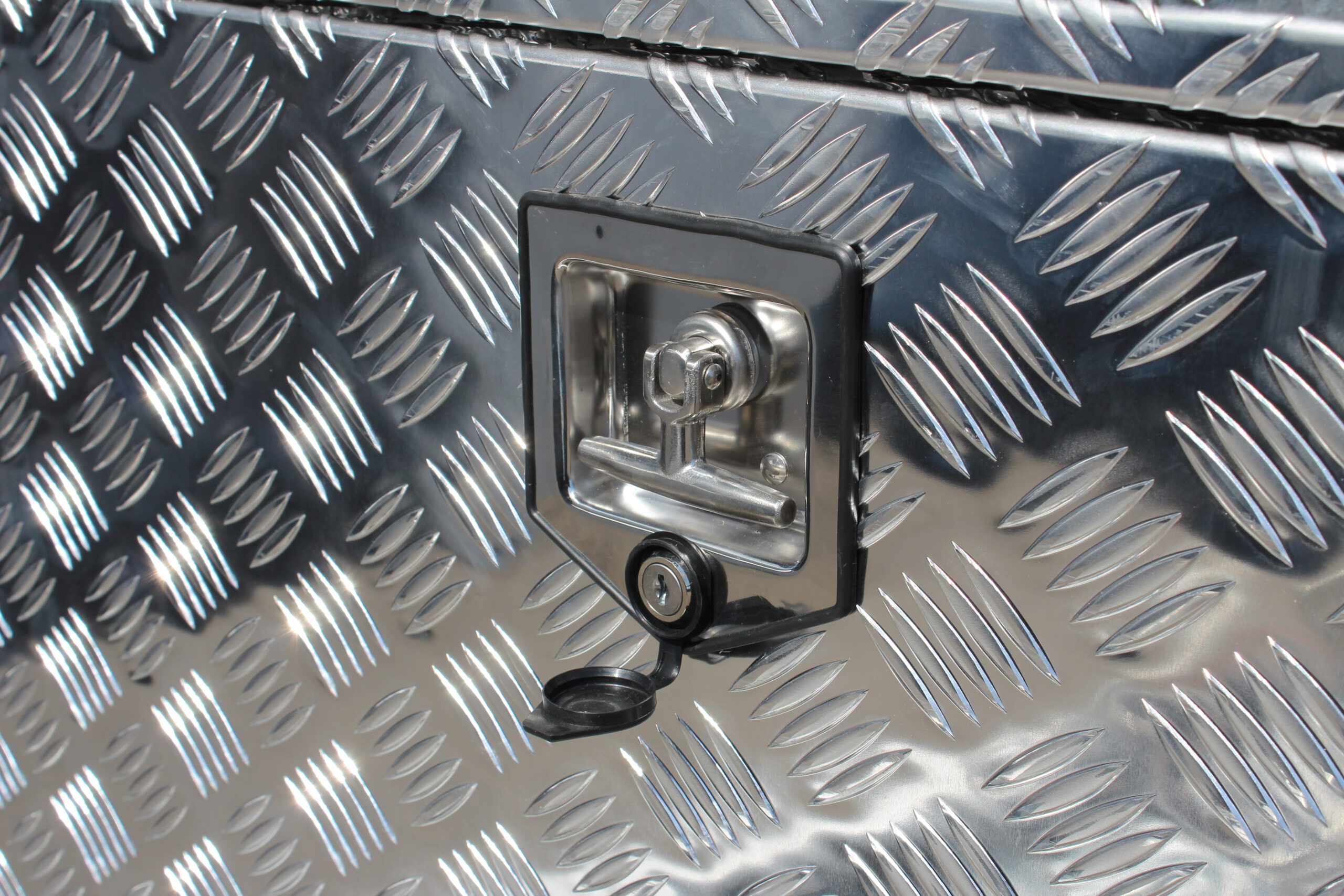 Große silberne Aluminium Riffelblech Staubox mit zwei Drehverschlüssen. Steht auf einem silbernen Aluminium Anhänger vor einem Tor